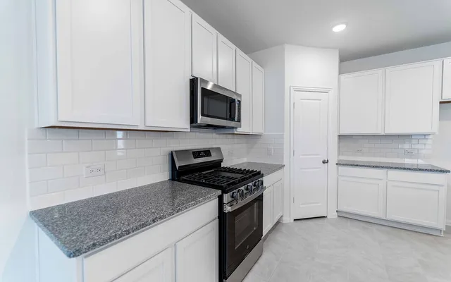 a kitchen with granite countertop white cabinets and a stove with wooden floor