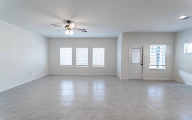 an empty room with chandelier fan and windows