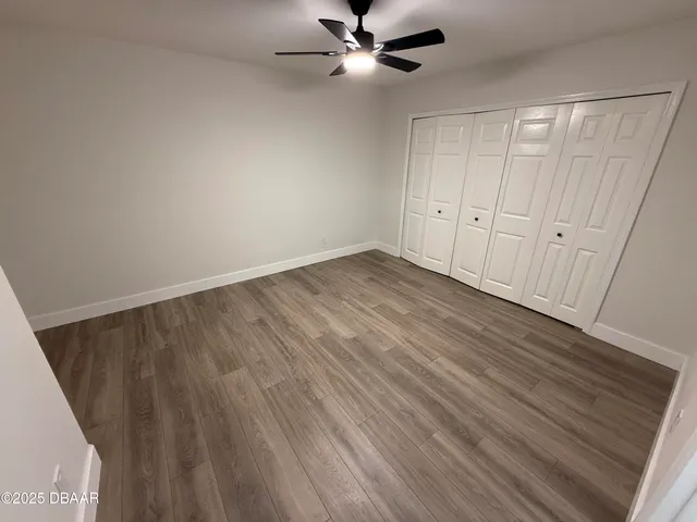 an empty room with wooden floor fan and windows