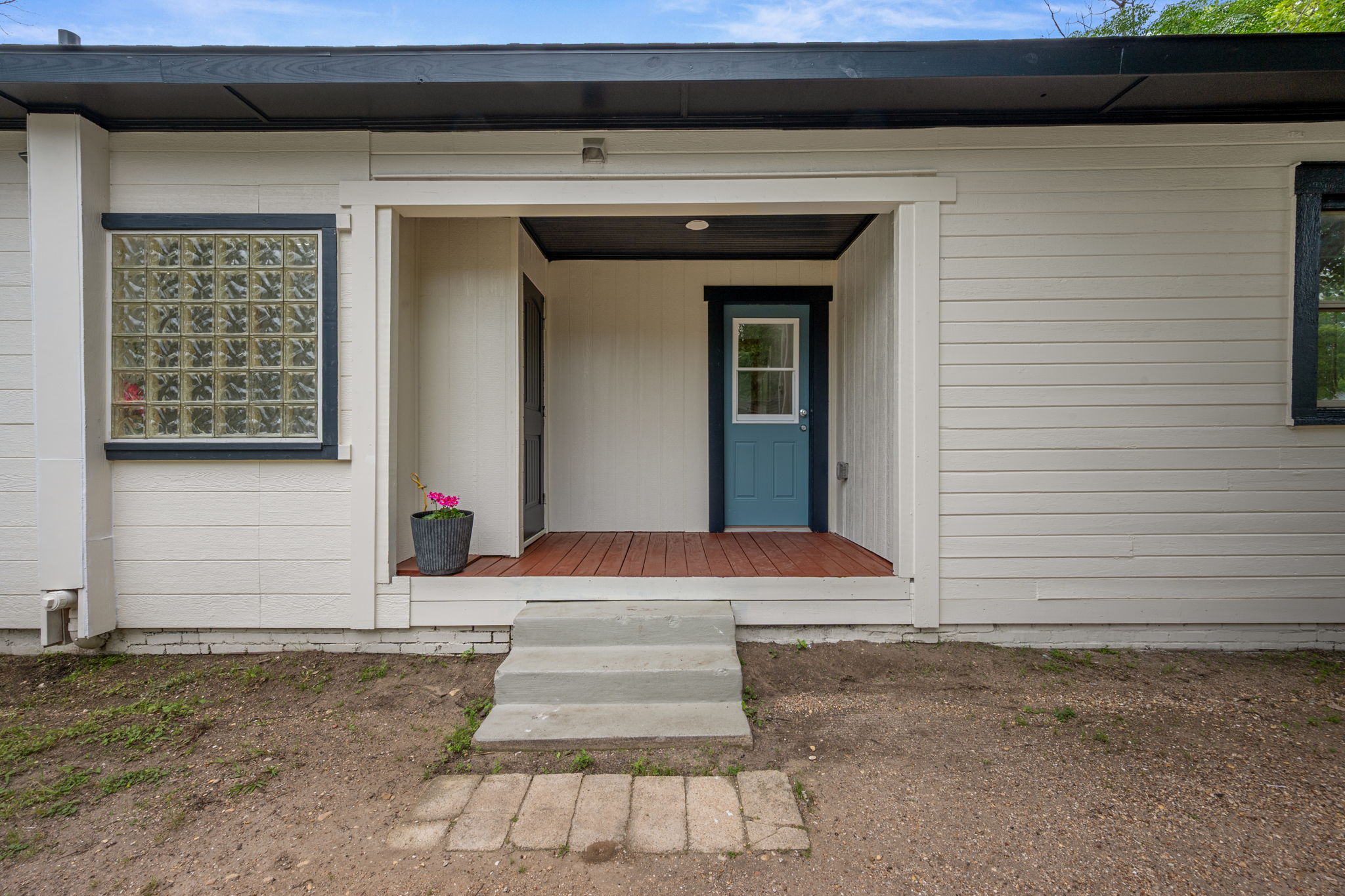 602 East 6th Street Cameron, TX 76520 - Photo 34 of 40 Exterior featuring horizontal siding in a light tone, a covered entry with a rich wood-finish deck, a distinctive blue entry door, and a glass block window