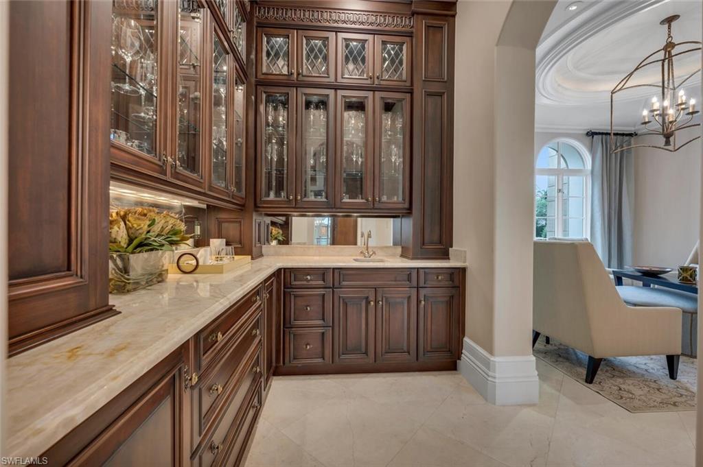 2125 Canna Way Naples, FL 34105 - Photo 14 of 43 Bar featuring glass insert cabinets, dark brown cabinetry, decorative light fixtures, light stone countertops, and a chandelier