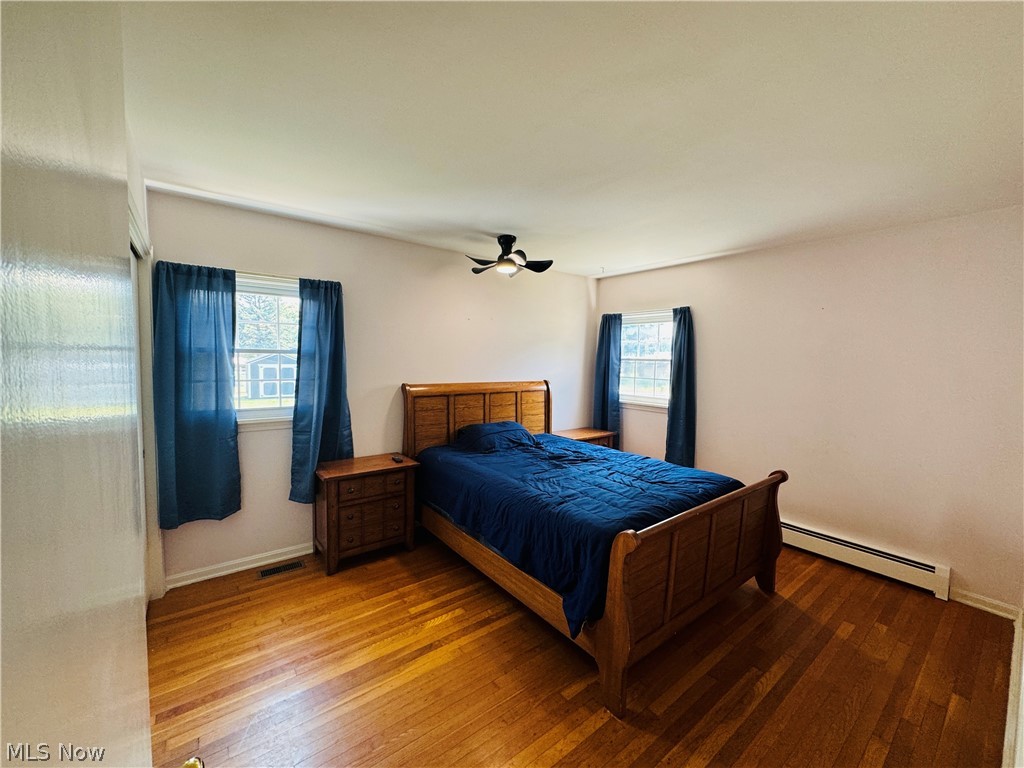 9531 West Ridge Road Elyria, OH 44035 - Photo 13 of 32 1st floor Bedroom with ceiling fan, multiple windows, baseboard heating, and wood-type flooring