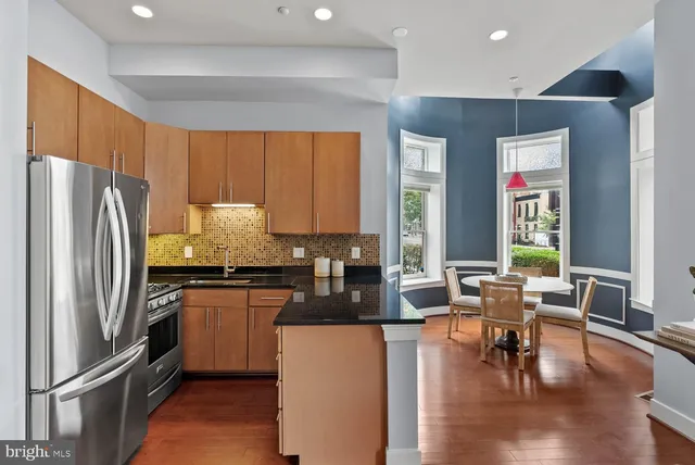 a kitchen with stainless steel appliances granite countertop a refrigerator a stove a sink a dining table and chairs with wooden floor