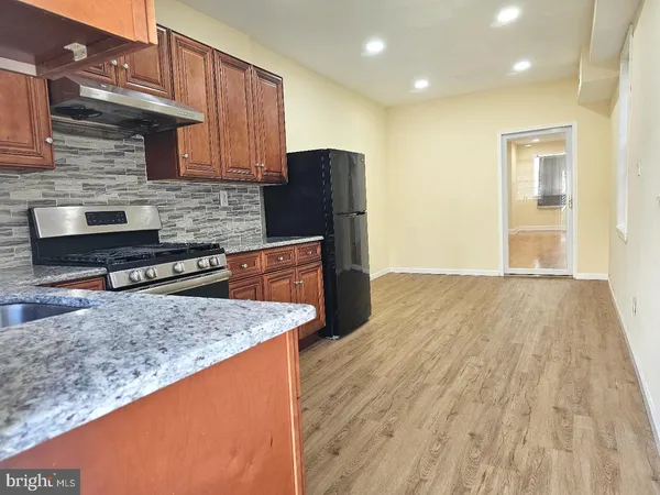 a kitchen with stainless steel appliances granite countertop wooden cabinets a refrigerator a sink and wooden floors