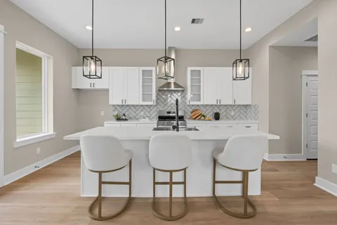 a large white kitchen with a large center island wooden floor and stainless steel appliances