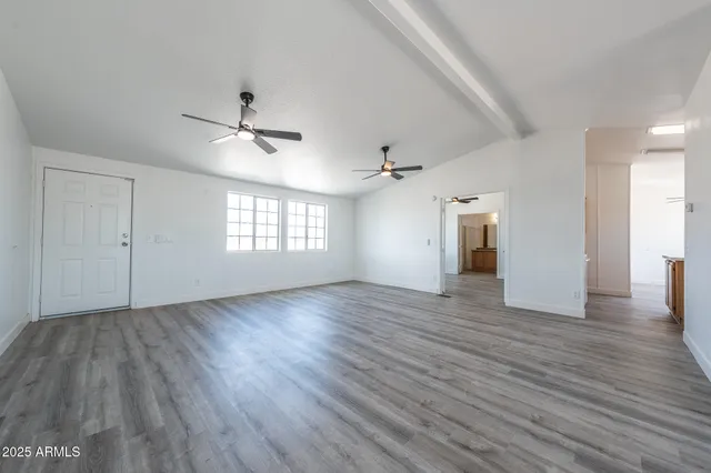 an empty room with wooden floor ceiling fan and windows