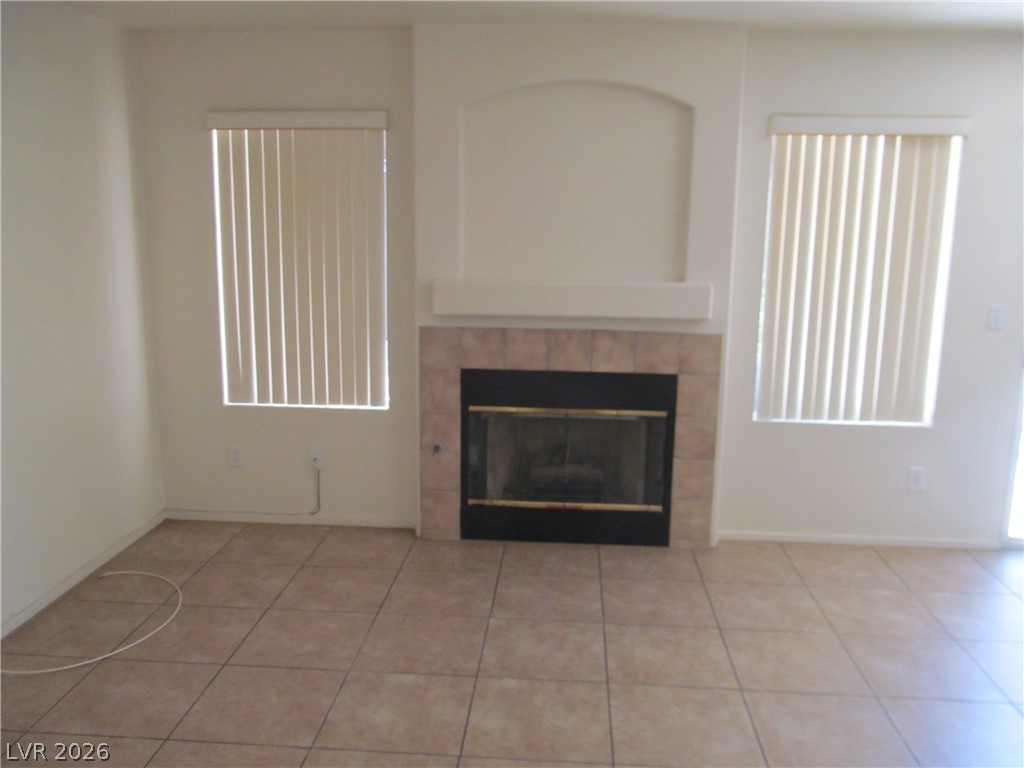 8701 Crescent Ridge Lane Las Vegas, NV 89134 - Photo 13 of 28 A well-lit room featuring a central fireplace with tiled surround and warm-toned flooring.