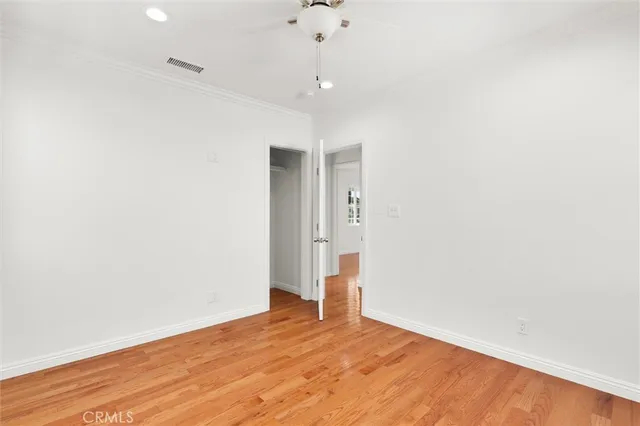 a view of an empty room with wooden floor and a ceiling fan