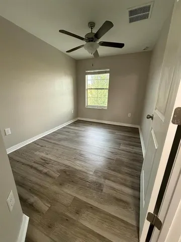 an empty room with wooden floor fan and windows