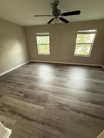 an empty room with wooden floor chandelier fan and windows