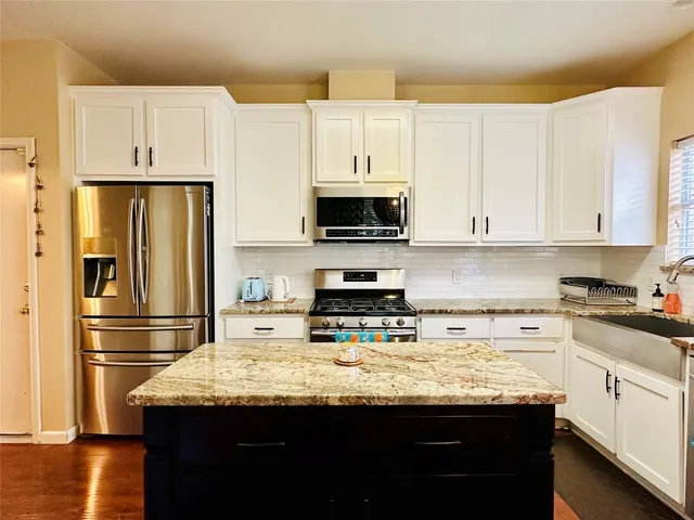 a kitchen with granite countertop a refrigerator stove and white cabinets