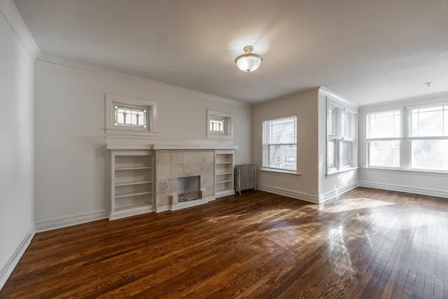 an empty room with wooden floor fireplace and windows