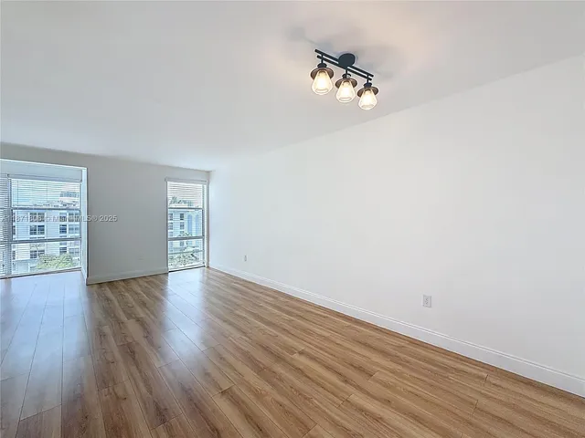an empty room with wooden floor cabinet and windows