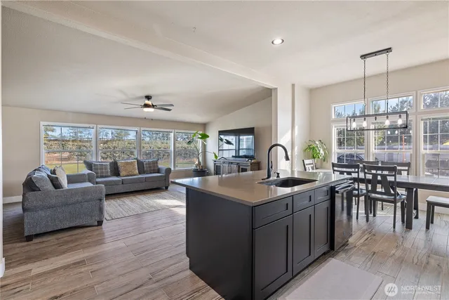 a open kitchen with stainless steel appliances granite countertop a sink dishwasher a stove and a dining table with wooden floor