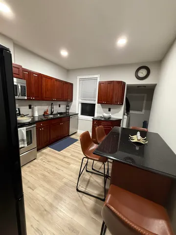 a kitchen with stainless steel appliances kitchen island granite countertop a sink dishwasher a stove a refrigerator a microwave oven with cabinets and wooden floor