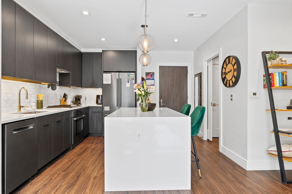 99 Sumner Street, Unit 101 Boston, MA 02128 - Photo 5 of 35 a kitchen with a refrigerator a stove top oven a clock and wooden floor