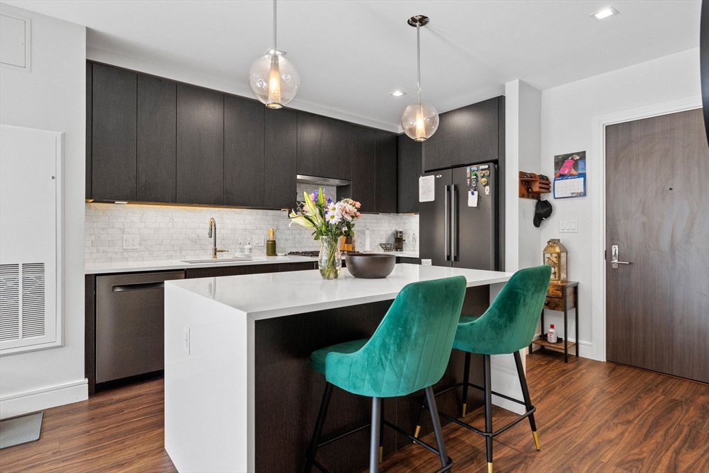 99 Sumner Street, Unit 101 Boston, MA 02128 - Photo 7 of 35 a kitchen with kitchen island a dining table chairs stainless steel appliances and wooden floor