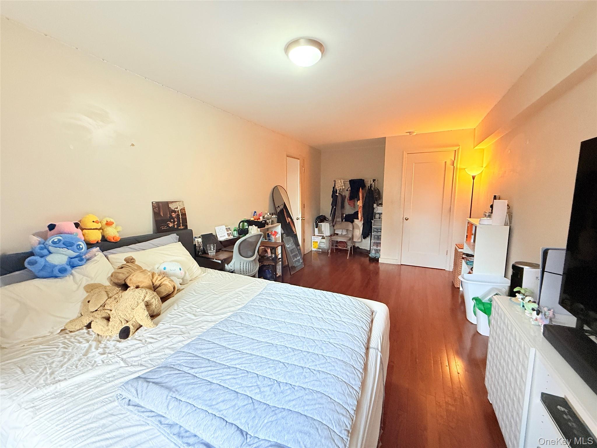87-10 51st Avenue, Unit 5H Queens, NY 11373 - Photo 5 of 16 a bed room with a bed and a flat tv screen on a dresser
