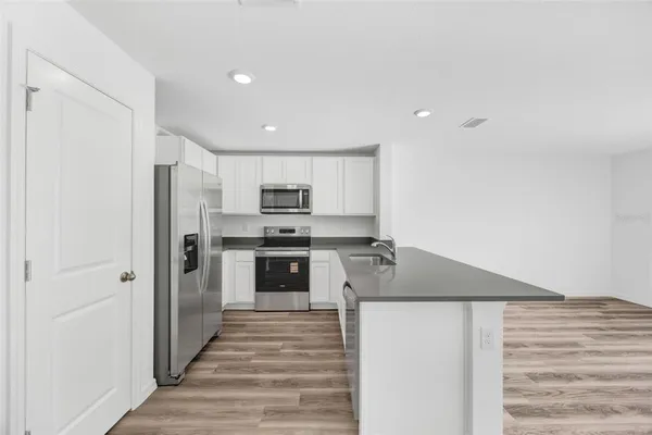 a kitchen with stainless steel appliances granite countertop a refrigerator oven a sink dishwasher and white cabinets with wooden floor