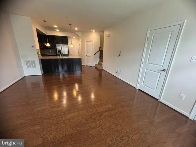 an empty room with wooden floor and kitchen view