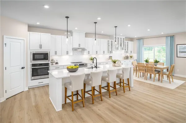 a kitchen with stainless steel appliances kitchen island granite countertop a table chairs stove and white cabinets