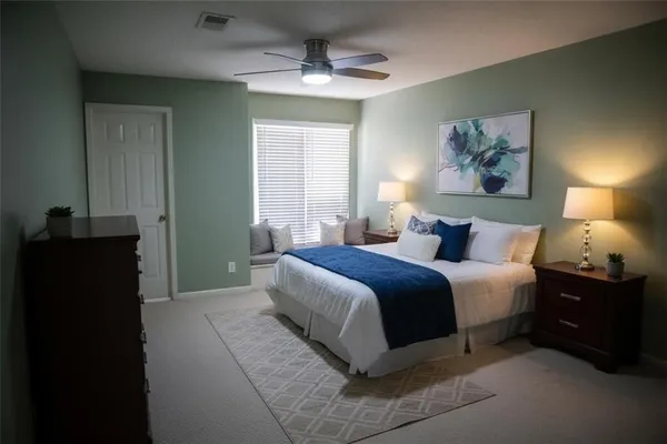 a spacious bedroom with a bed and a lamp on dresser