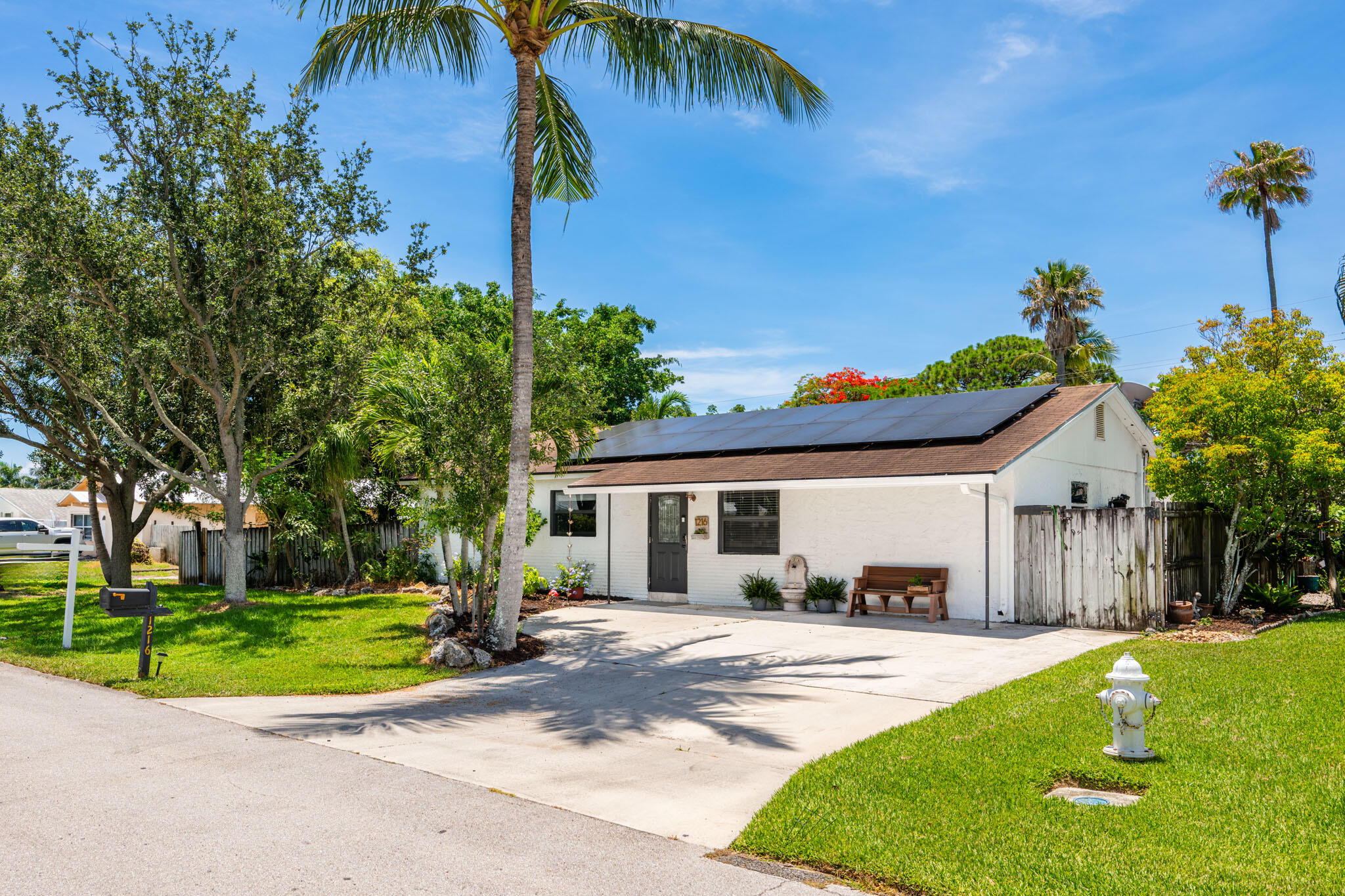 1216 Neoga Street Jupiter, FL 33458 - Photo 2 of 27 a view of a white house with a swimming pool and a lawn chairs under palm trees