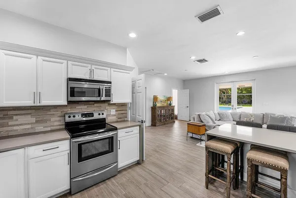 a open kitchen with stainless steel appliances kitchen island granite countertop a stove top oven a sink a dining table and chairs with wooden floor