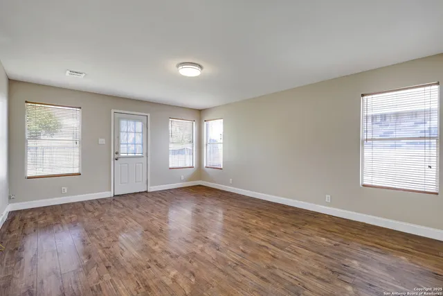 a view of an empty room with wooden floor and a window