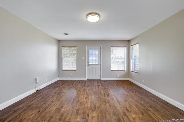 a view of an empty room with wooden floor and a window