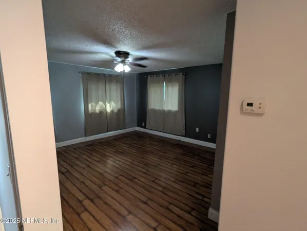 a view of an empty room with wooden floor and a ceiling fan