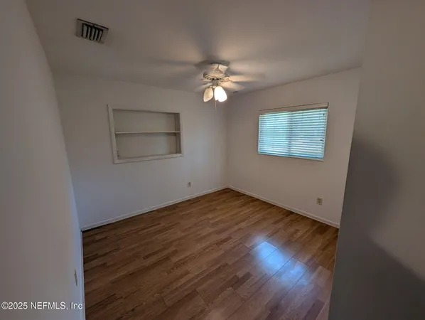an empty room with wooden floor ceiling fan and windows