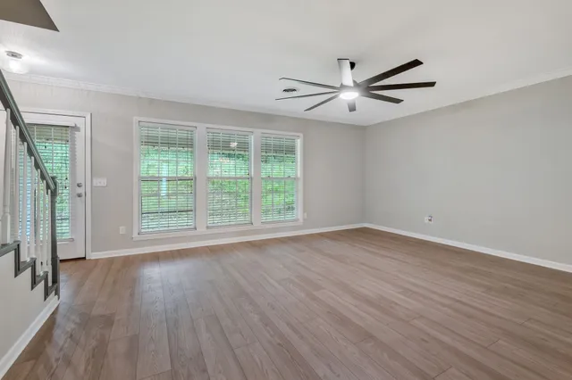 an empty room with wooden floor fan and windows