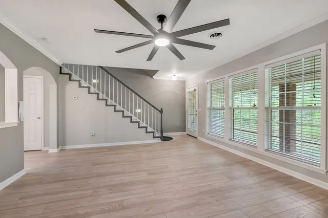 a view of an empty room with wooden floor and a ceiling fan