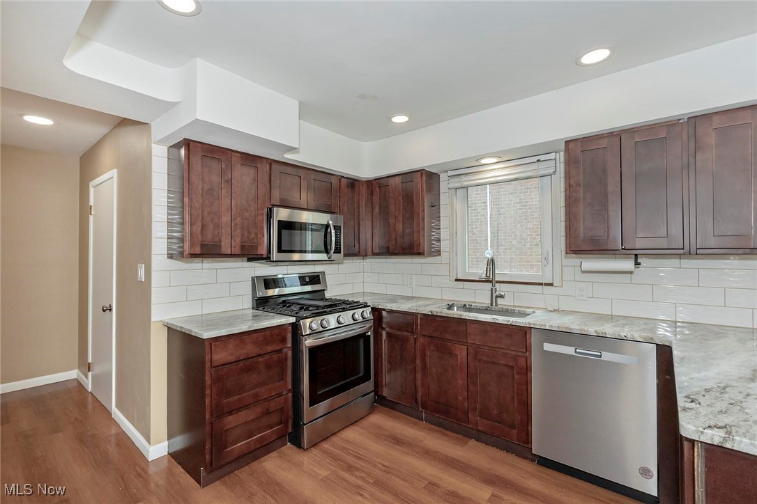 2381 Charney Road Cleveland, OH 44118 - Photo 5 of 47 Kitchen featuring appliances with stainless steel finishes, a sink, light wood-style flooring, baseboards, and light stone countertops and lots of storage