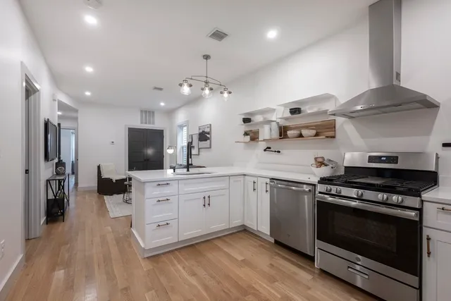 a kitchen with stainless steel appliances a stove top oven a sink dishwasher and a refrigerator with wooden floor