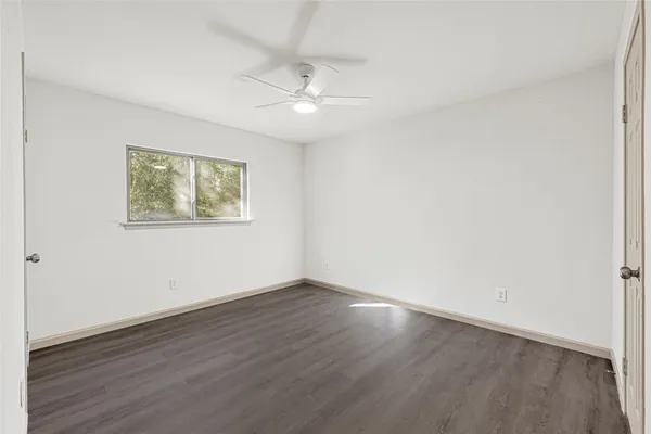 a view of an empty room with wooden floor and a ceiling fan