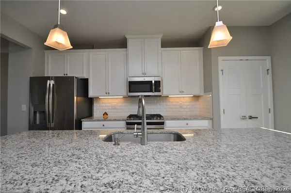a large white kitchen with stainless steel appliances granite countertop a stove a sink a refrigerator and a dining table with wooden floor