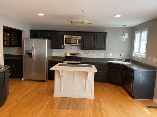 a kitchen with stainless steel appliances granite countertop a sink a stove a refrigerator cabinets and a wooden floor