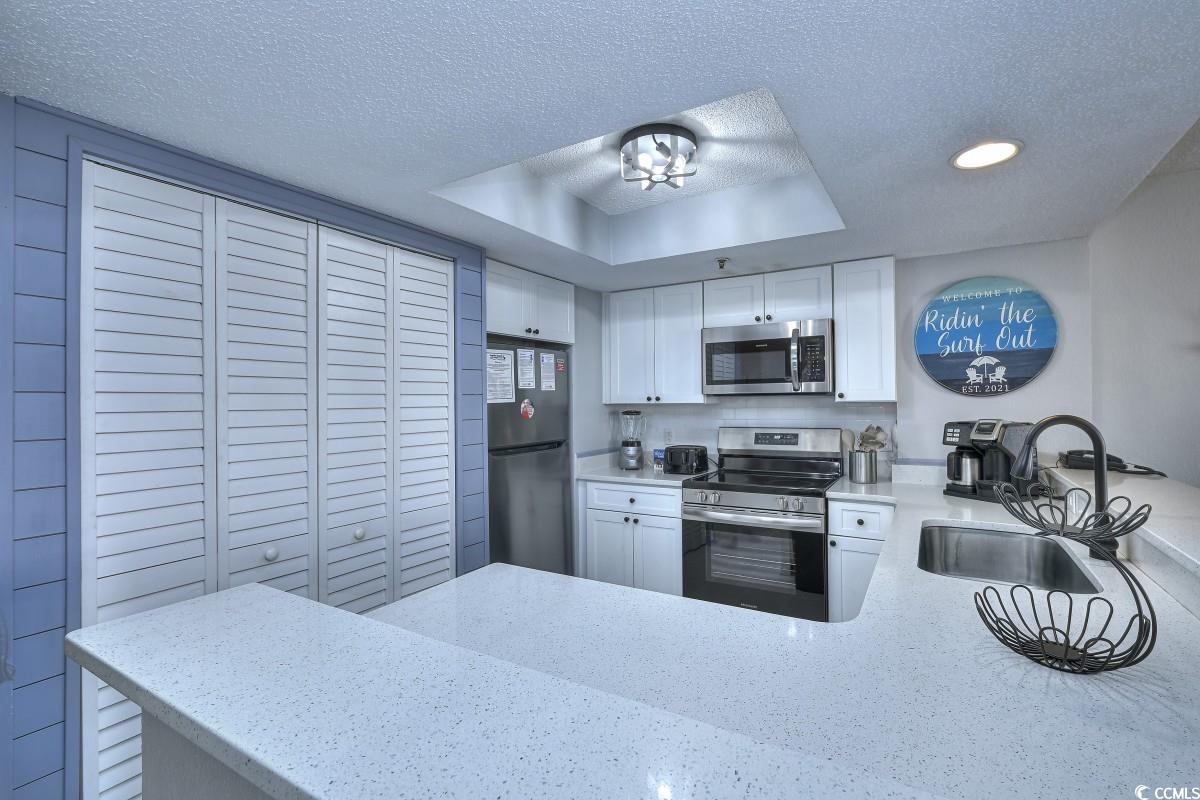 2311 South Ocean Boulevard, Unit 624 Myrtle Beach, SC 29577 - Photo 2 of 28 Kitchen featuring appliances with stainless steel finishes, a textured ceiling, a tray ceiling, white cabinets, and a peninsula
