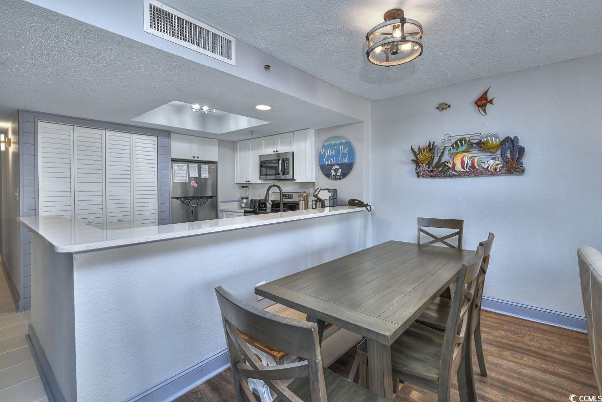 2311 South Ocean Boulevard, Unit 624 Myrtle Beach, SC 29577 - Photo 3 of 28 Dining room featuring a textured ceiling, modern light/ceiling fan and dark wood-style floors. Wood table with bench seating and chairs and artwork.