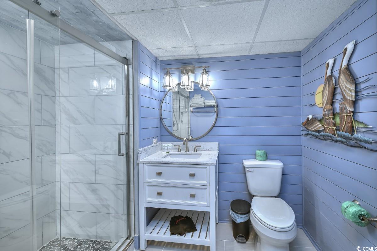 2311 South Ocean Boulevard, Unit 624 Myrtle Beach, SC 29577 - Photo 5 of 28 Bathroom featuring a drop ceiling, vanity, walk-in tile shower with pebbled floor, and shiplap walls.