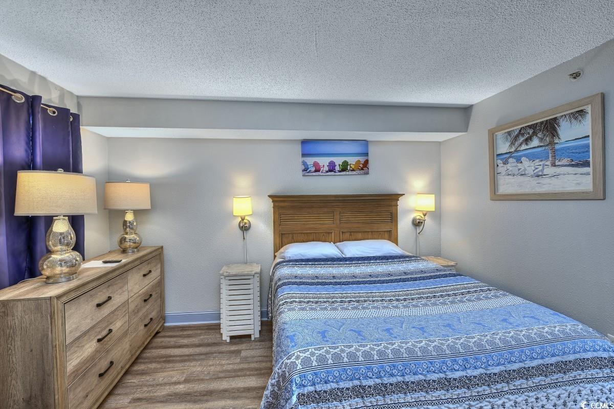 2311 South Ocean Boulevard, Unit 624 Myrtle Beach, SC 29577 - Photo 8 of 28 Bedroom featuring a textured ceiling and dark wood-style floors. Artwork, bed, dresser, and two night stands.