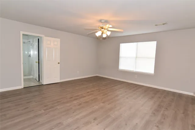 an empty room with wooden floor chandelier fan and windows