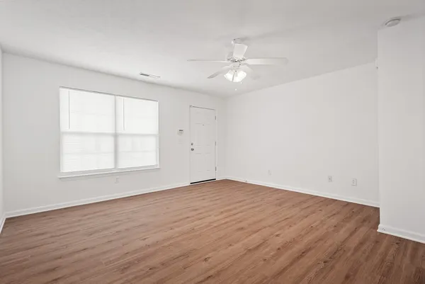 an empty room with wooden floor fan and windows