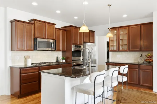 a kitchen with stainless steel appliances granite countertop a stove a sink a microwave a refrigerator white cabinets and wooden floor
