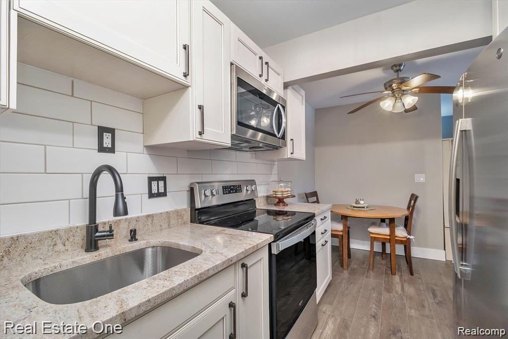 803 Plate Street, Unit 104 Rochester, MI 48307 - Photo 9 of 14 Kitchen featuring off white shaker cabinetry, stainless steel appliances, a subway tile backsplash, and wood-finish flooring