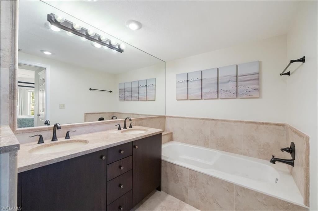 6025 Chardonnay Lane, Unit 103 Naples, FL 34119 - Photo 27 of 45 a bathroom with a tub a double vanity sink and mirror