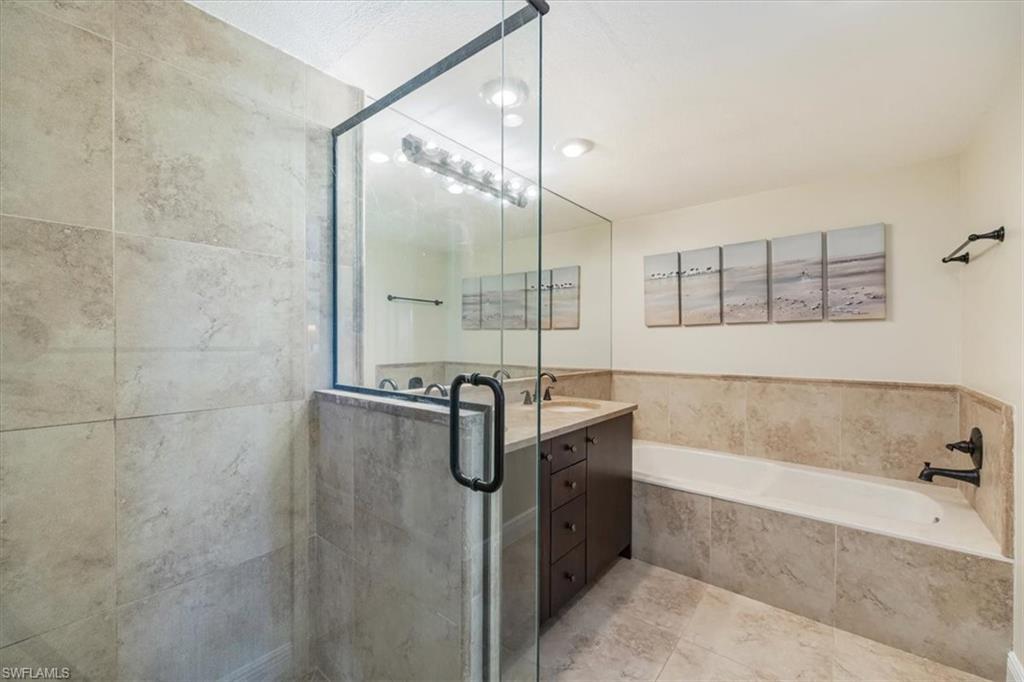 6025 Chardonnay Lane, Unit 103 Naples, FL 34119 - Photo 29 of 45 a bathroom with a tub a sink a mirror and a shower