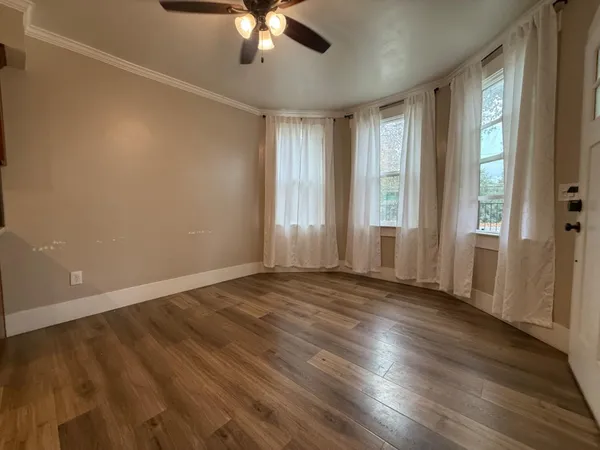 an empty room with wooden floor fan and windows
